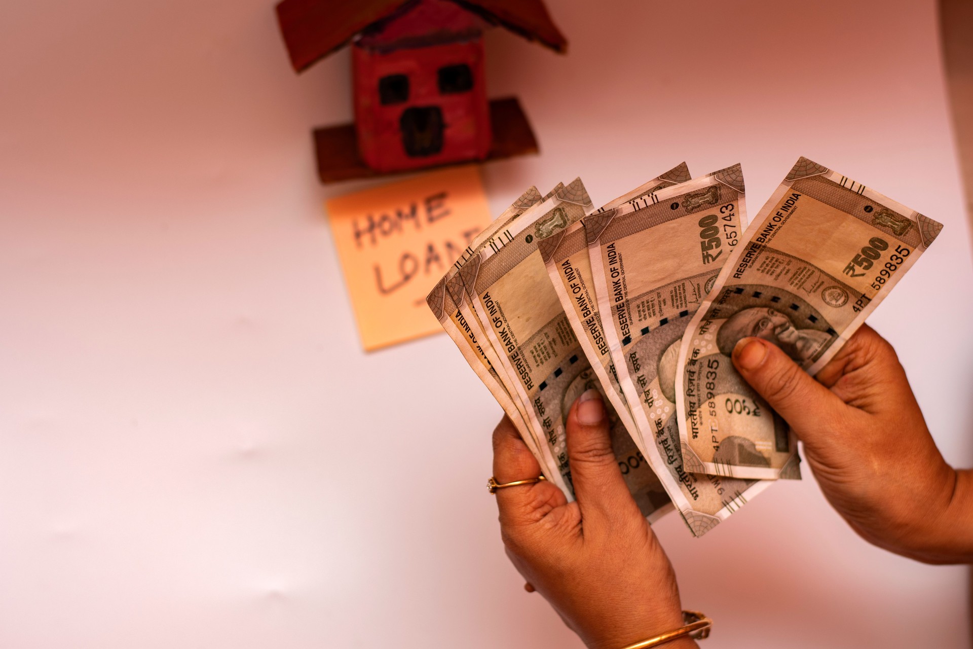 Woman Counting Savings for Home Loan EMI with Handcrafted Hut and Note